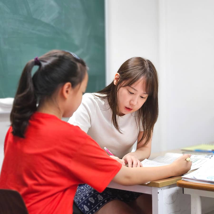선생님이 학생 옆에서 문제 풀이 과정을 함께 확인하는 모습