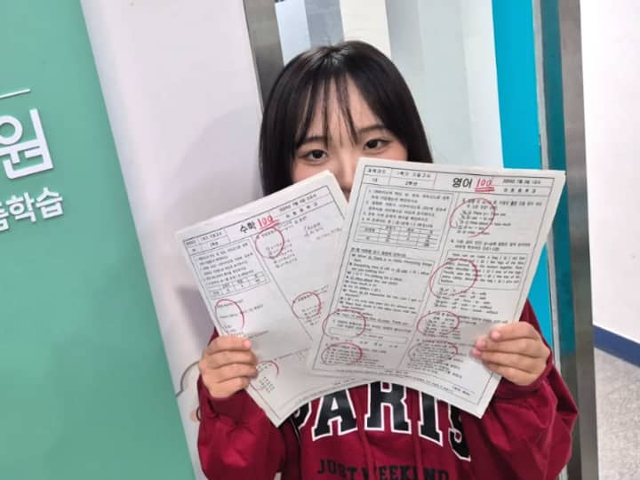한맥학원 로고 앞에서 수학 100점, 영어 100점 시험지를 든 학생