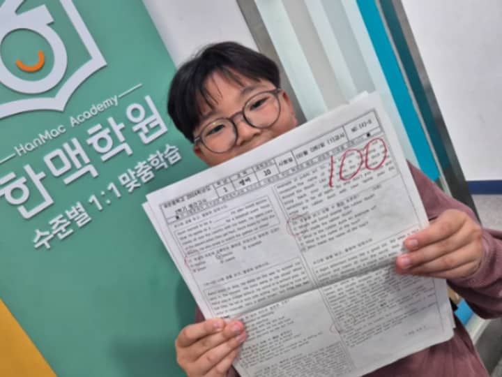 한맥학원 로고 앞에서 100점 시험지를 든 학생